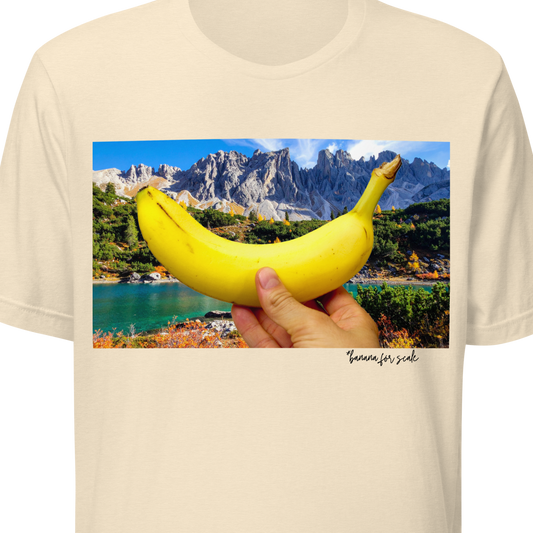 Beige t-shirt with a scenic print of a hand holding a banana over a mountain lake.