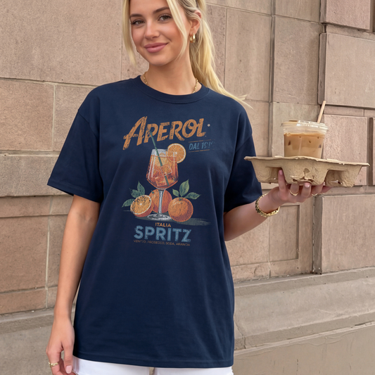 Woman wearing a navy blue t-shirt with Aperol Spritz design, holding a drink.