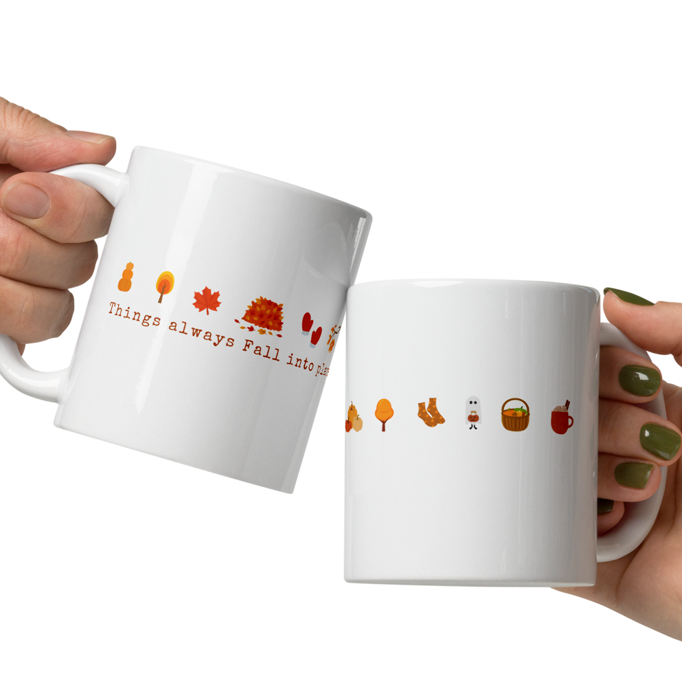 Two white mugs with autumn-themed illustrations and text held by two hands.