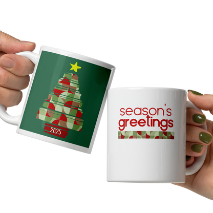 Two hands holding Christmas-themed mugs with tree and 'season's greetings' designs.