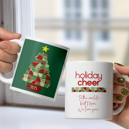 Two mugs, one with a Christmas tree design and the other with 'holiday cheer' text, held by hands.