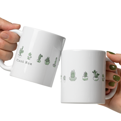 Two white mugs with plant-themed designs held by hands against a white background