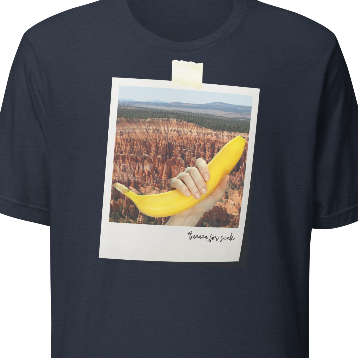Navy blue t-shirt with a graphic of a hand holding a banana over a scenic landscape, pinned to a white background.