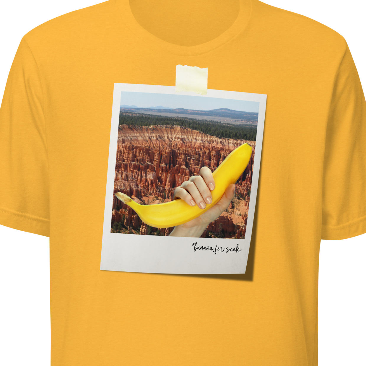 Yellow t-shirt with a graphic of a hand holding a banana over a scenic landscape, on a white background.
