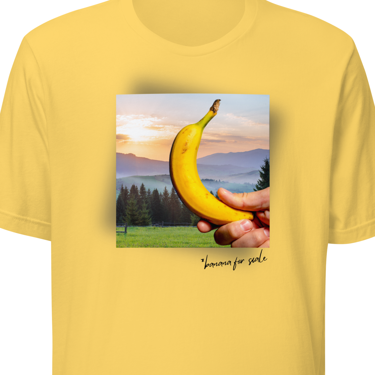 Yellow t-shirt with a graphic of a hand holding a banana and a sunset over trees on a white background