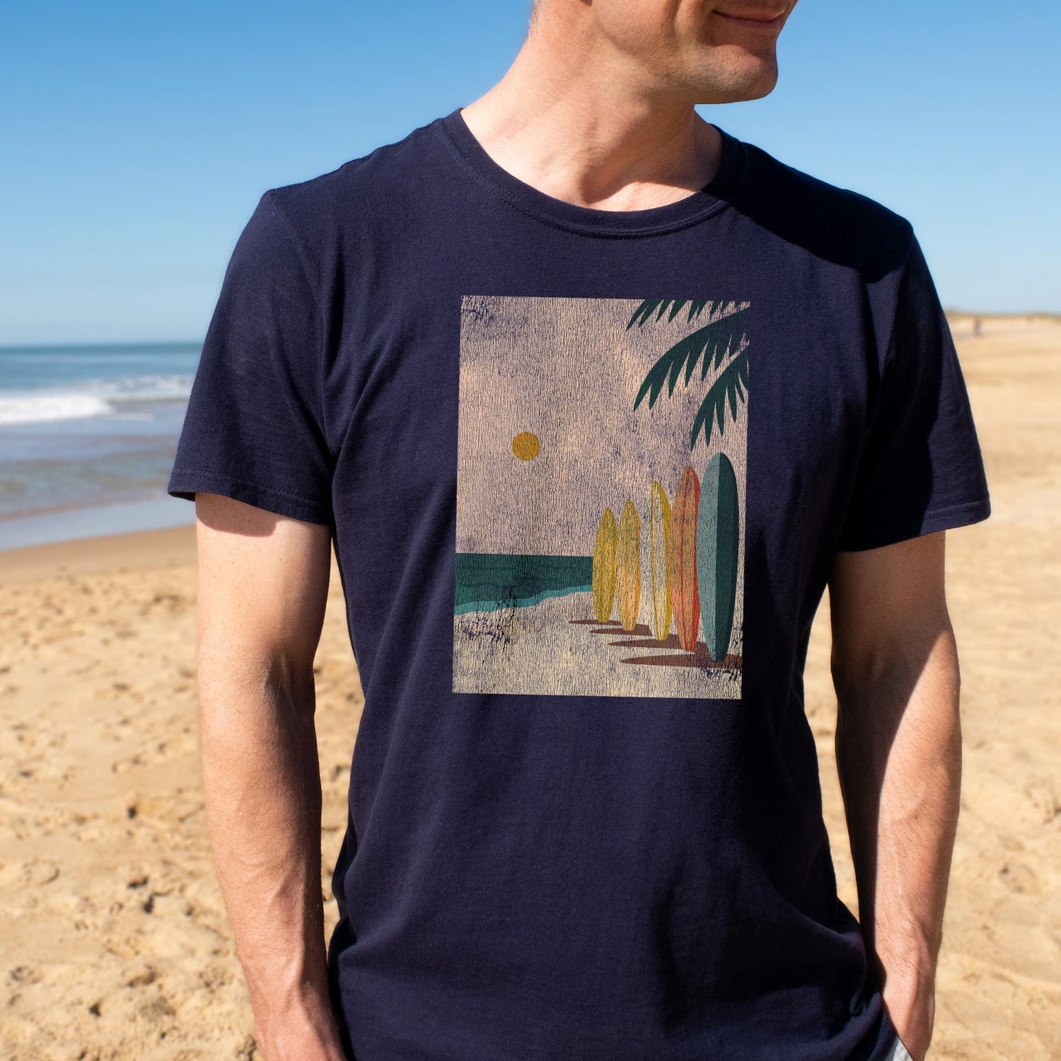Person wearing a navy blue t-shirt with a beach graphic on a sandy beach.